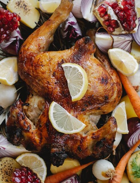 Overhead of tasty grilled whole chicken with lemon and pomegranate placed among onion with carrot served in glass bowl on towel